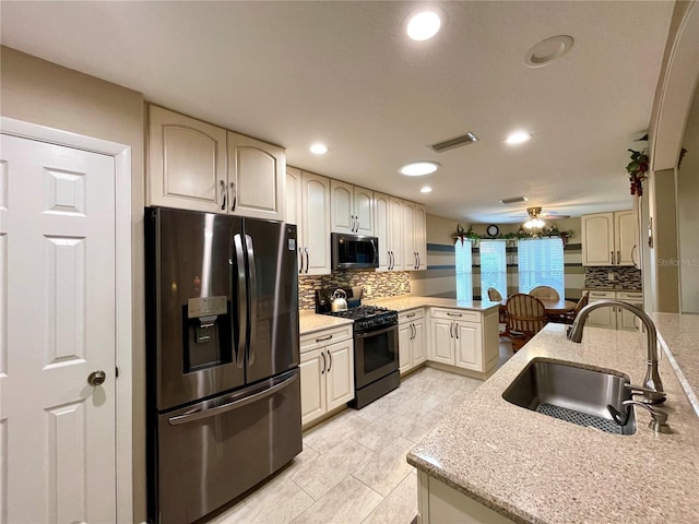 kitchen featuring stainless steel fridge with ice dispenser, light stone countertops, black gas range, sink, and tasteful backsplash