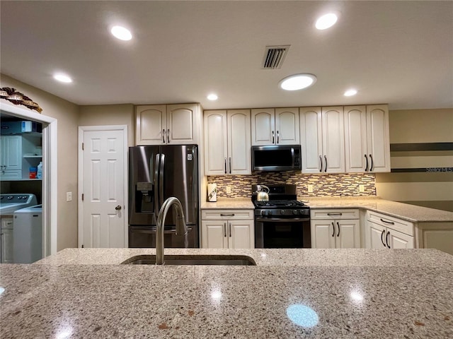 kitchen featuring light stone counters, independent washer and dryer, gas stove, sink, and stainless steel fridge with ice dispenser