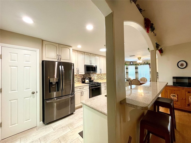 kitchen with a breakfast bar, light stone countertops, tasteful backsplash, ceiling fan, and appliances with stainless steel finishes