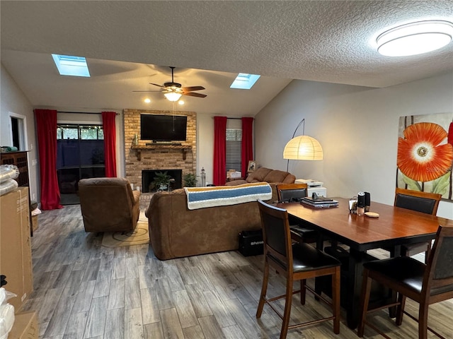 dining area featuring a textured ceiling, a fireplace, hardwood / wood-style flooring, ceiling fan, and lofted ceiling with skylight