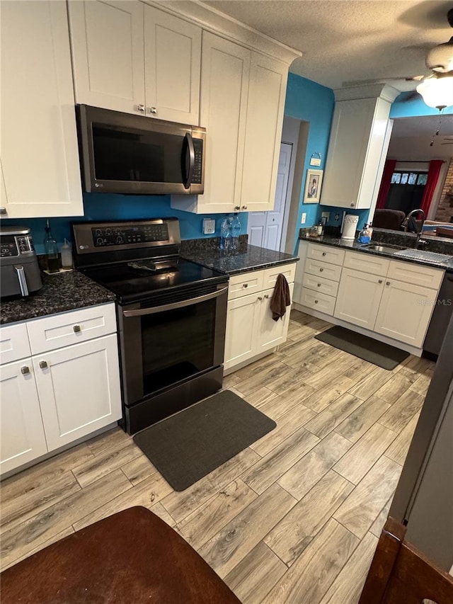 kitchen with white cabinetry, stainless steel appliances, dark stone counters, a textured ceiling, and sink