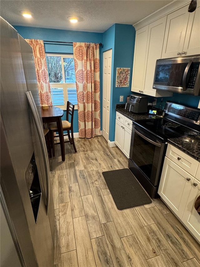 kitchen with appliances with stainless steel finishes, dark stone counters, white cabinetry, and a textured ceiling