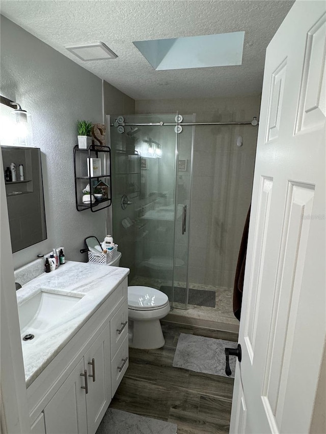 bathroom featuring toilet, a skylight, hardwood / wood-style flooring, walk in shower, and vanity