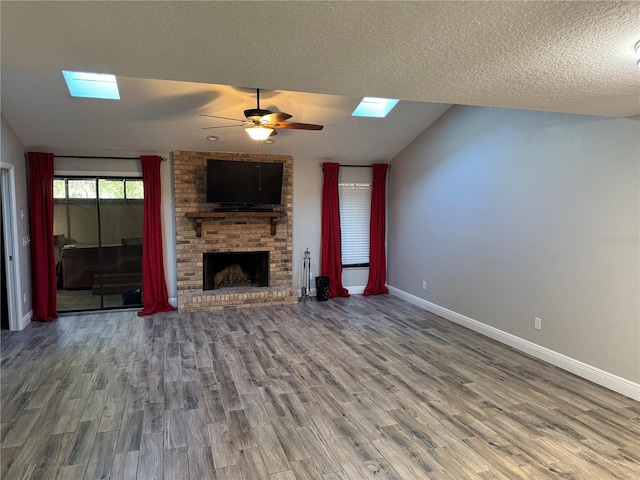 unfurnished living room featuring hardwood / wood-style flooring, ceiling fan, a textured ceiling, a brick fireplace, and vaulted ceiling