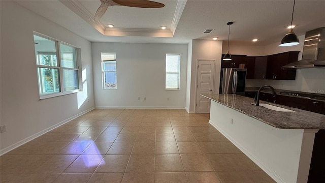 kitchen featuring sink, stainless steel fridge, dark stone countertops, range hood, and a tray ceiling