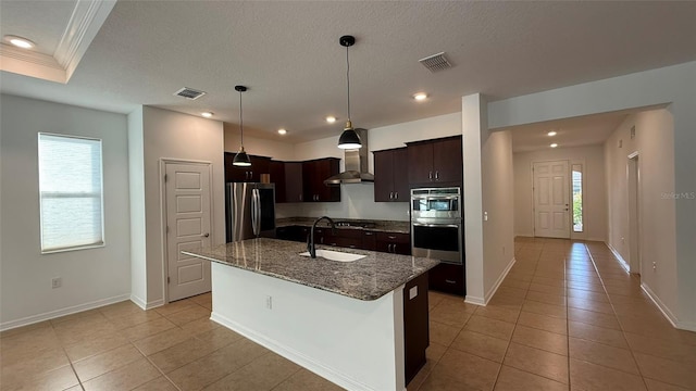 kitchen featuring appliances with stainless steel finishes, sink, a kitchen island with sink, dark brown cabinets, and wall chimney exhaust hood