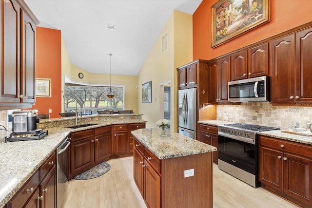 kitchen with sink, light stone counters, tasteful backsplash, decorative light fixtures, and appliances with stainless steel finishes