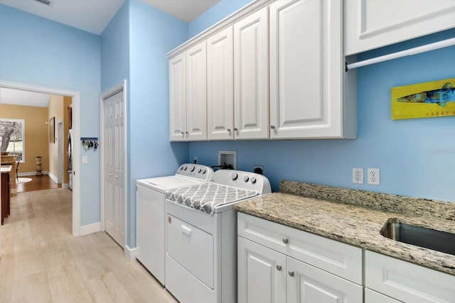 clothes washing area featuring light hardwood / wood-style flooring, cabinets, and washing machine and clothes dryer