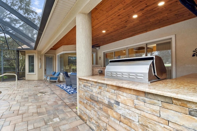 view of patio featuring an outdoor kitchen, exterior bar, area for grilling, and glass enclosure