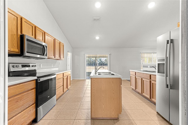 kitchen with lofted ceiling, sink, light tile patterned floors, appliances with stainless steel finishes, and a kitchen island with sink