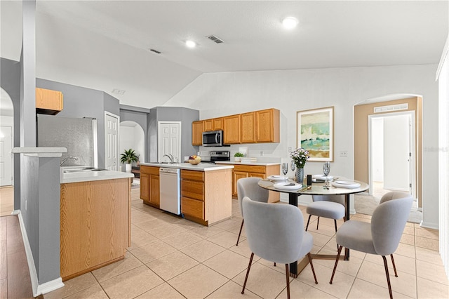 kitchen with light tile patterned floors, sink, appliances with stainless steel finishes, a center island with sink, and vaulted ceiling