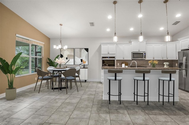 kitchen featuring lofted ceiling, a breakfast bar area, white cabinets, hanging light fixtures, and stainless steel appliances