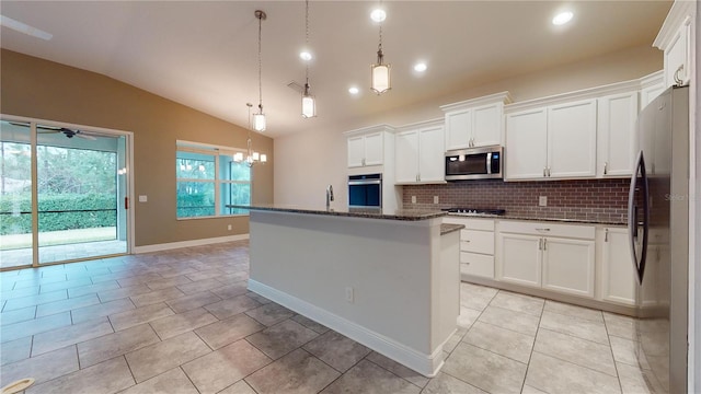 kitchen with appliances with stainless steel finishes, decorative light fixtures, white cabinetry, backsplash, and a center island with sink