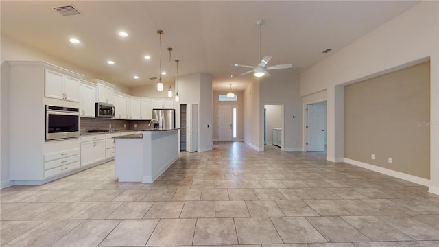 kitchen with tasteful backsplash, a center island with sink, appliances with stainless steel finishes, pendant lighting, and white cabinets