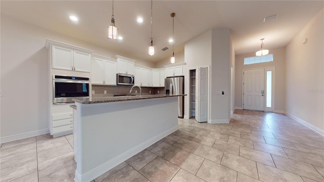 kitchen with appliances with stainless steel finishes, white cabinetry, dark stone countertops, decorative backsplash, and a center island with sink