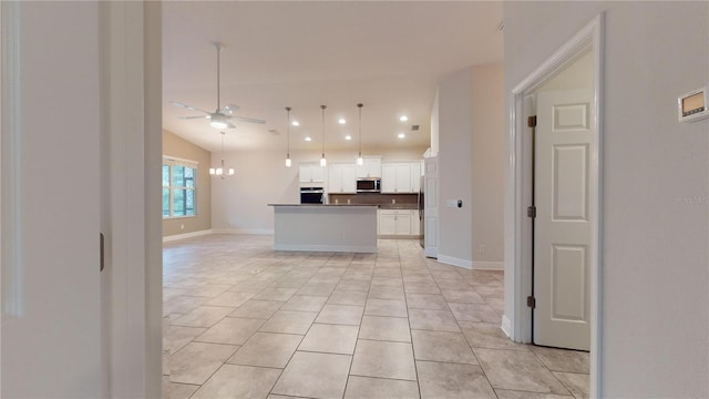 kitchen with light tile patterned flooring, a kitchen island, appliances with stainless steel finishes, ceiling fan with notable chandelier, and white cabinetry