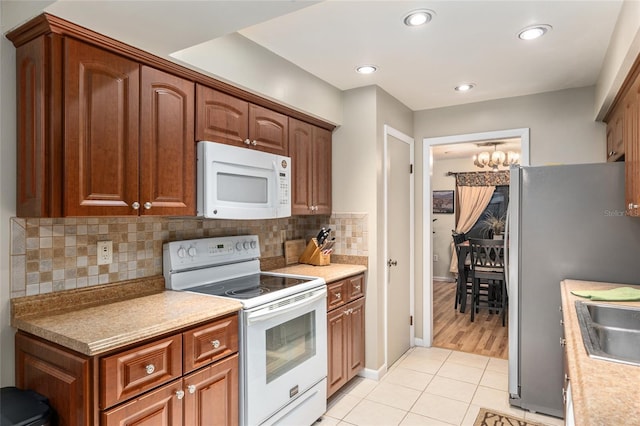 kitchen featuring backsplash, white appliances, light tile patterned floors, and a chandelier