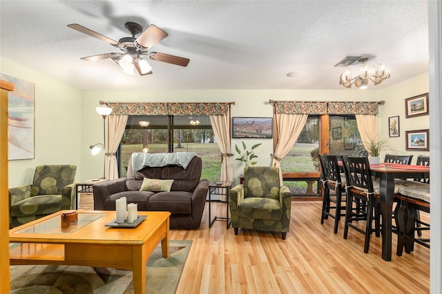 living room featuring light wood-type flooring, a textured ceiling, and ceiling fan with notable chandelier