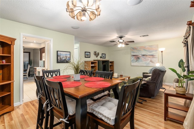 dining area with ceiling fan with notable chandelier, a textured ceiling, and light hardwood / wood-style flooring