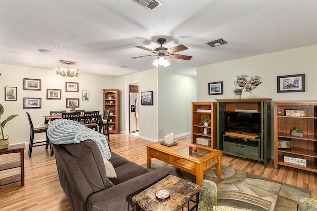 living room featuring ceiling fan with notable chandelier, a textured ceiling, and light hardwood / wood-style flooring