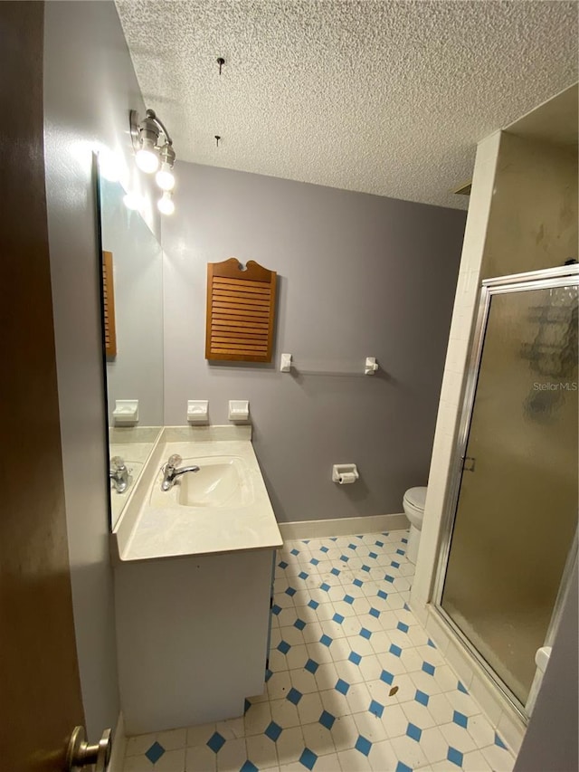 bathroom featuring a textured ceiling, toilet, a shower with door, and vanity