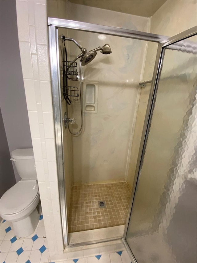 bathroom featuring toilet, tile patterned floors, and a shower with door