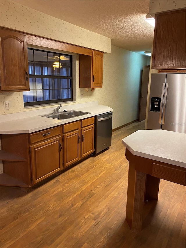 kitchen with light wood-type flooring, appliances with stainless steel finishes, sink, and a textured ceiling