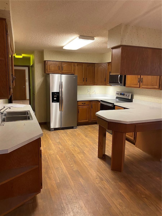 kitchen featuring kitchen peninsula, stainless steel appliances, light wood-type flooring, a textured ceiling, and sink