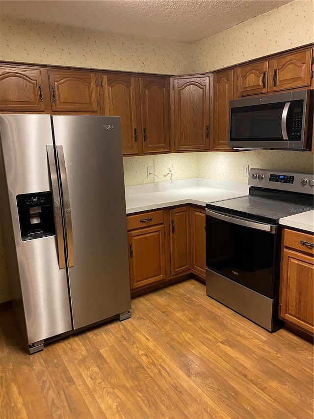 kitchen featuring a textured ceiling, appliances with stainless steel finishes, and light hardwood / wood-style flooring