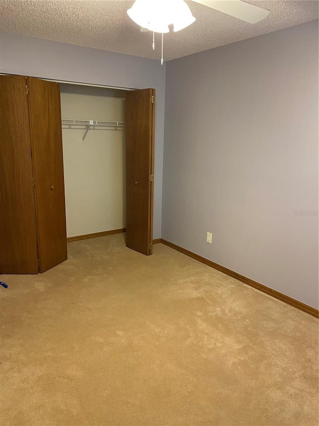 unfurnished bedroom featuring a textured ceiling, a closet, light carpet, and ceiling fan