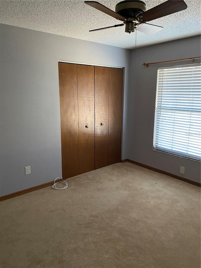 unfurnished bedroom with a textured ceiling, ceiling fan, a closet, and light colored carpet