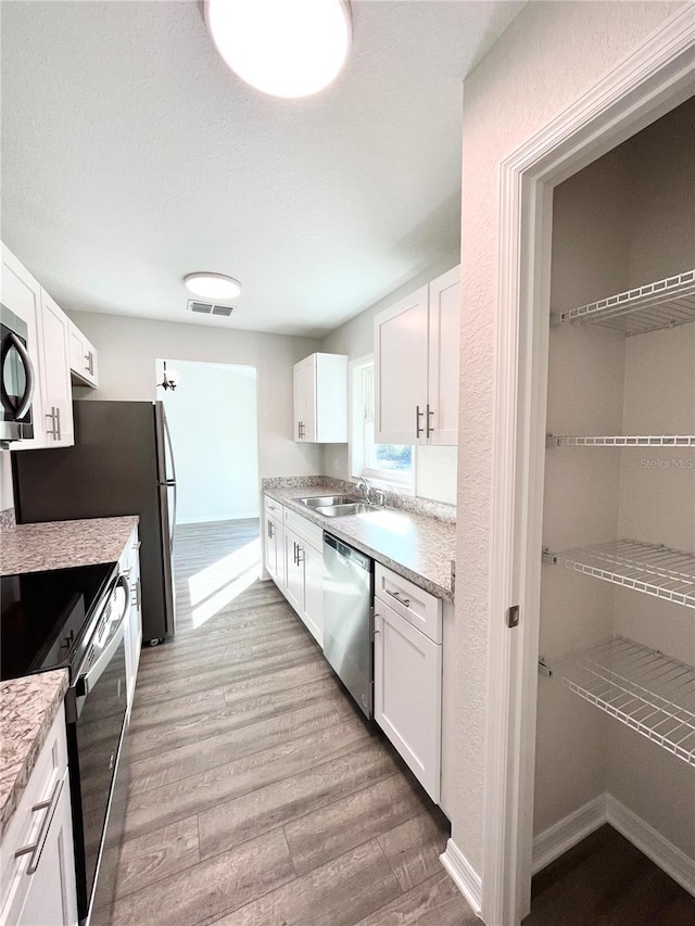 kitchen with sink, white cabinets, stainless steel appliances, and light wood-type flooring