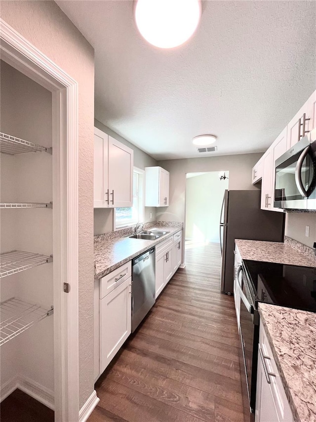 kitchen featuring dark hardwood / wood-style floors, sink, stainless steel appliances, a textured ceiling, and white cabinets