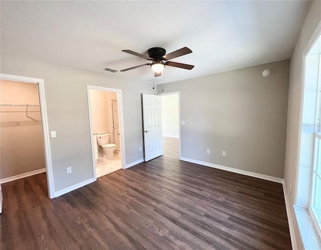 unfurnished bedroom featuring a spacious closet, ceiling fan, connected bathroom, a closet, and dark wood-type flooring