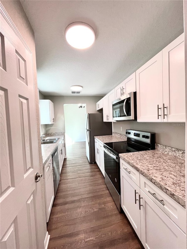 kitchen with white cabinetry, appliances with stainless steel finishes, dark wood-type flooring, light stone counters, and sink