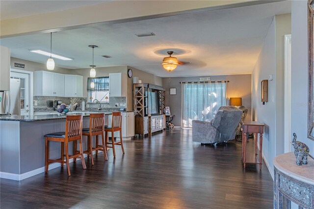 kitchen with pendant lighting, white cabinetry, backsplash, a kitchen bar, and dark wood-type flooring