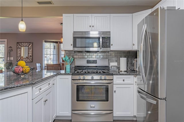 kitchen with dark stone countertops, appliances with stainless steel finishes, decorative light fixtures, and white cabinets