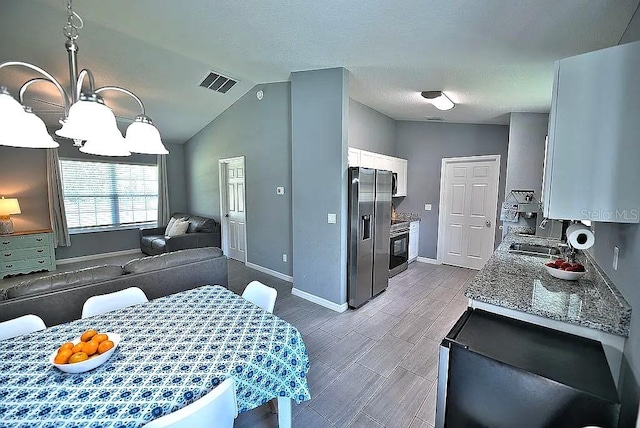 kitchen featuring light stone countertops, white cabinetry, pendant lighting, vaulted ceiling, and stainless steel fridge