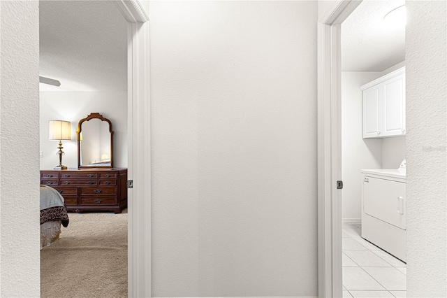 corridor featuring washer / dryer, a textured ceiling, and light tile patterned floors