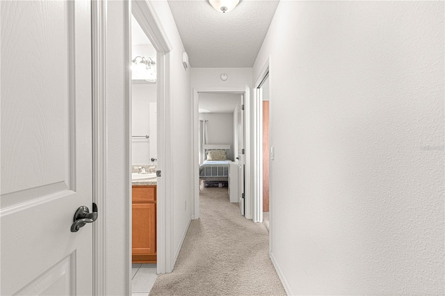 corridor featuring light carpet, sink, and a textured ceiling