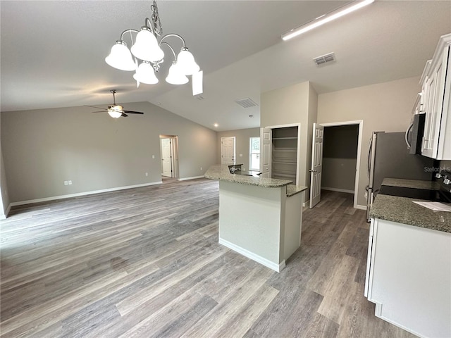 kitchen featuring ceiling fan with notable chandelier, white cabinets, decorative light fixtures, dark stone countertops, and vaulted ceiling