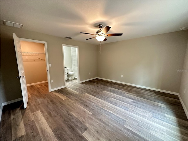 unfurnished bedroom featuring a spacious closet, wood-type flooring, connected bathroom, a closet, and ceiling fan