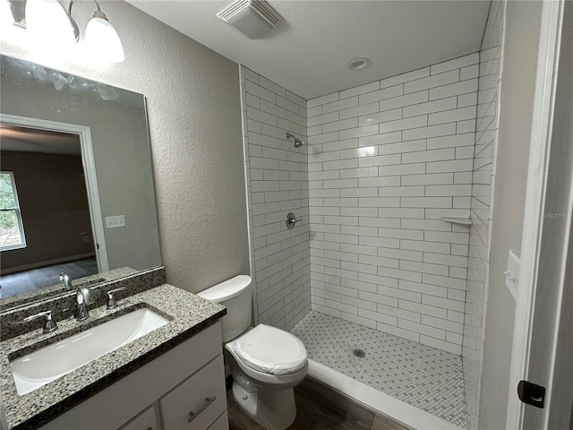 bathroom featuring toilet, a tile shower, and vanity