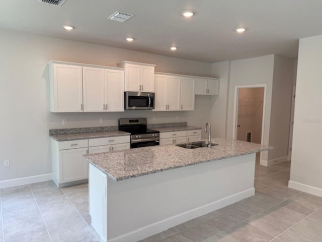 2214 NW 23rd Loop, Ocala, FL 34475 - kitchen with stainless steel appliances, white cabinets, light tile patterned floors, a center island with sink, and light stone countertops