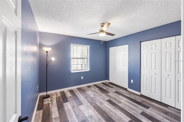 unfurnished bedroom with ceiling fan, two closets, a textured ceiling, and dark hardwood / wood-style flooring