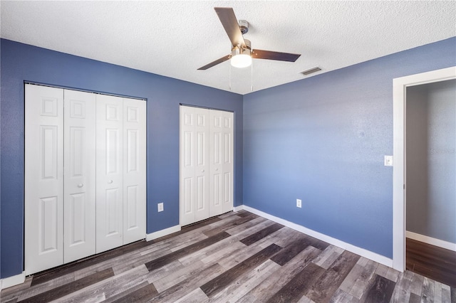 unfurnished bedroom with a textured ceiling, ceiling fan, dark hardwood / wood-style flooring, and multiple closets