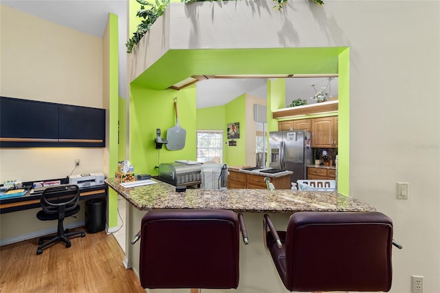 kitchen with stainless steel fridge, light stone countertops, kitchen peninsula, and a kitchen bar