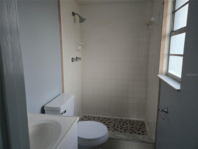 bathroom featuring toilet, vanity, plenty of natural light, and a tile shower