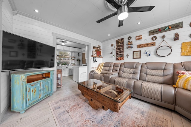 living room with light wood-type flooring, ceiling fan, crown molding, and wood walls