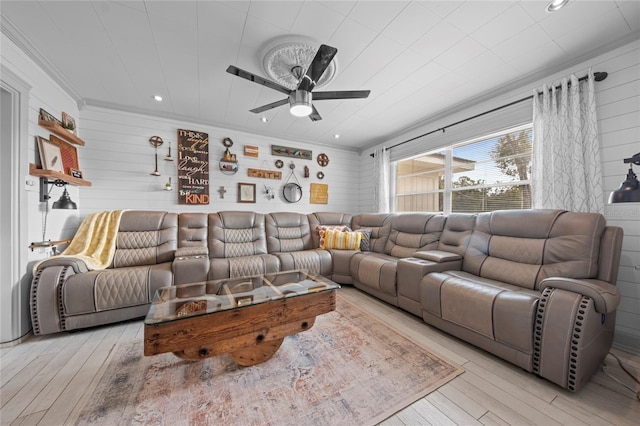 living room featuring ceiling fan, light wood-type flooring, wooden walls, and ornamental molding